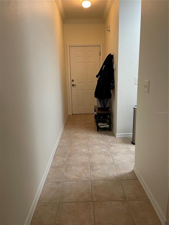 A tiled hallway leads to a white door with a coat rack and shoe storage — 9172 SW 52ND ROAD UNIT F202, GAINESVILLE, FL