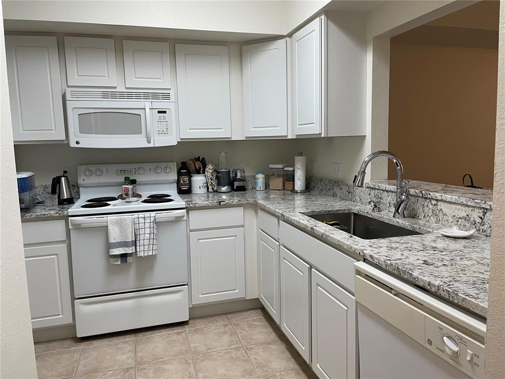 A kitchen features white cabinets, granite countertops, and white appliances — 9172 SW 52ND ROAD UNIT F202, GAINESVILLE, FL