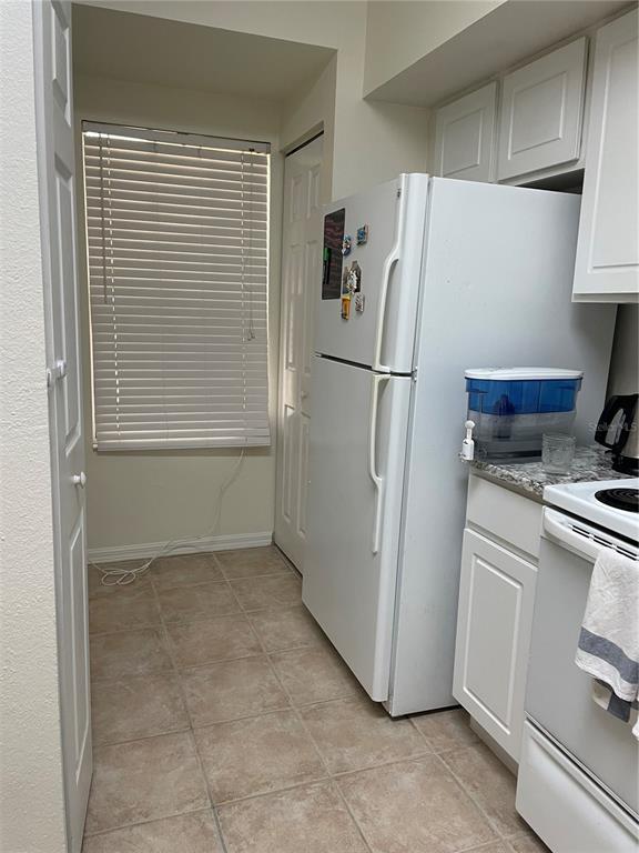 A kitchen features white cabinets, a white refrigerator, a window with blinds, and tile flooring — 9172 SW 52ND ROAD UNIT F202, GAINESVILLE, FL