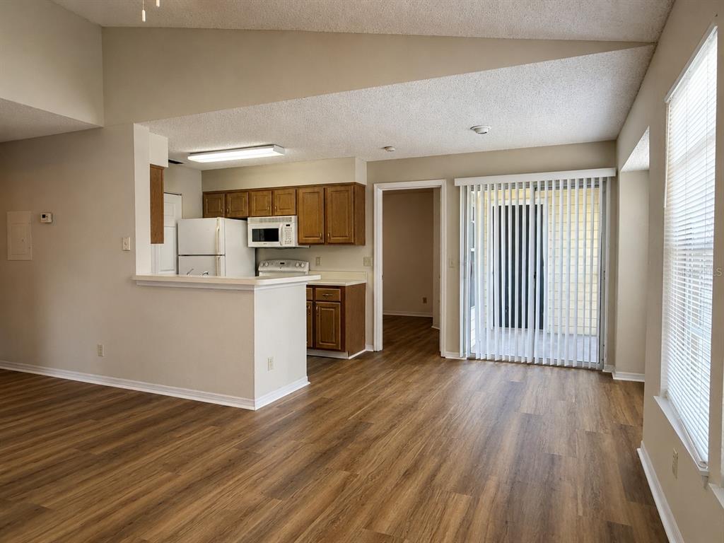 An open-concept kitchen with wood cabinets and a breakfast bar overlooks a living area — 1063 S HIAWASSEE ROAD UNIT 1628, ORLANDO, FL