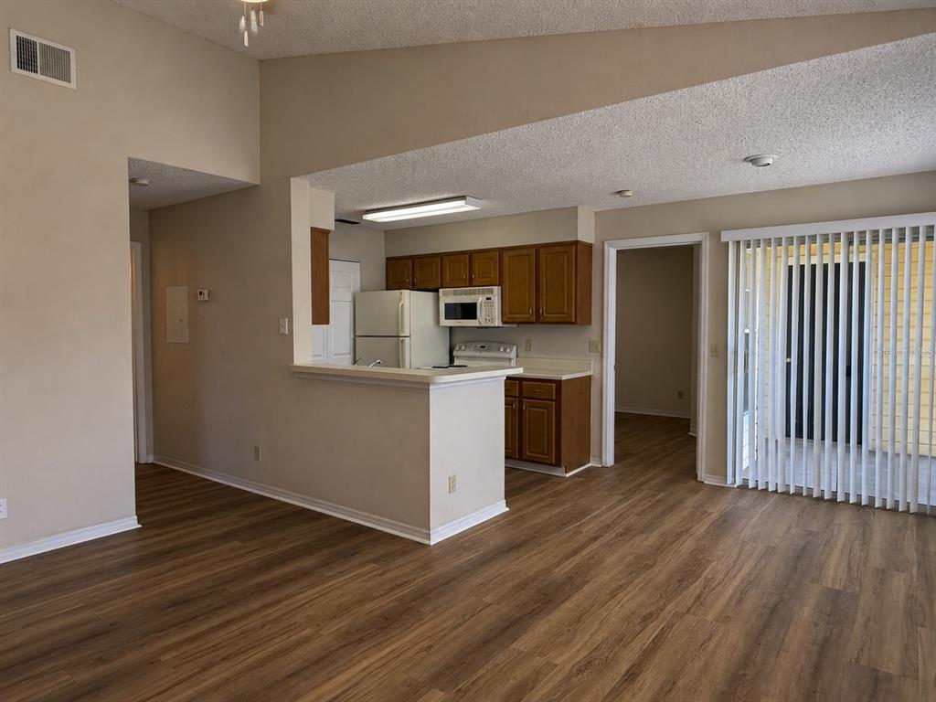 An open-concept kitchen with wood cabinets and a breakfast bar overlooks a living area — 1063 S HIAWASSEE ROAD UNIT 1628, ORLANDO, FL