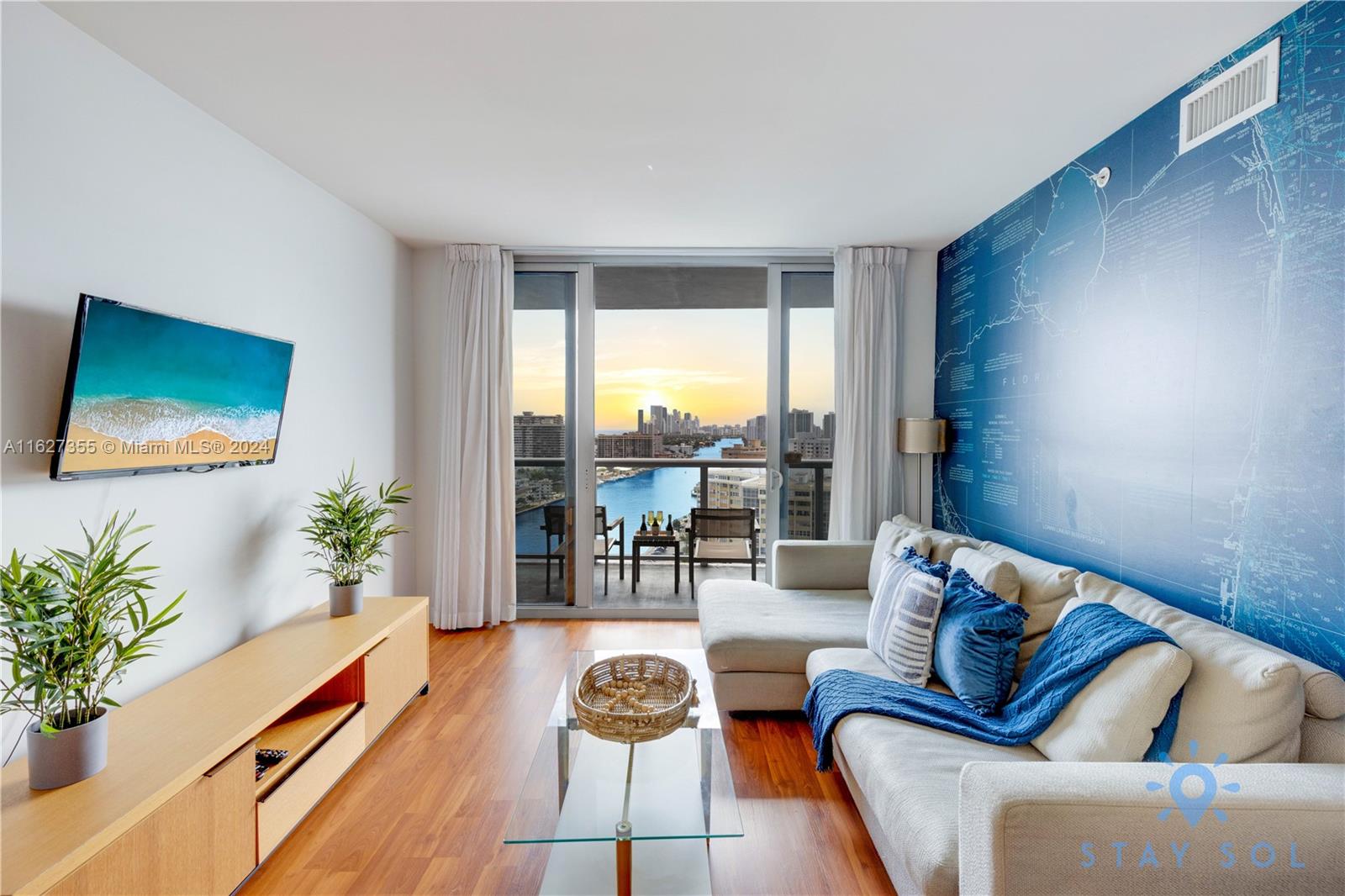 A living room features a blue map wall, a sectional sofa, and a balcony view — 2602 E Hallandale Beach Blvd # R2009, Hallandale Beach FL 33009, HALLANDALE BEACH, FL