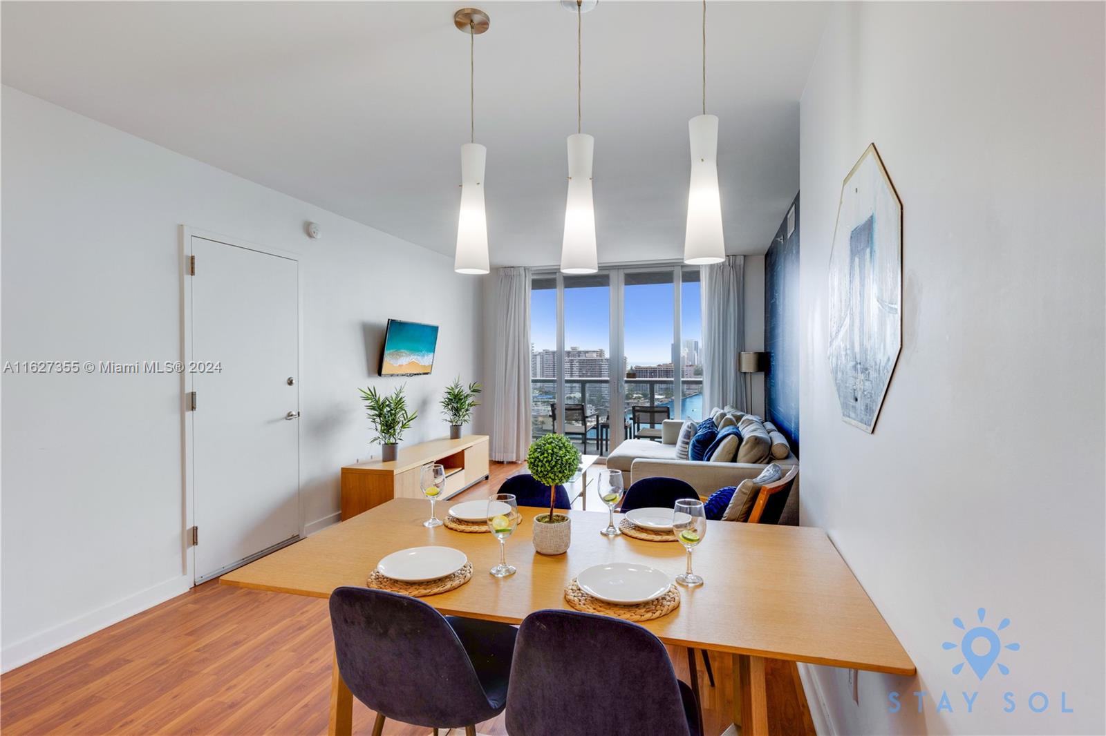 A dining area with a wooden table and chairs sits before a living room balcony — 2602 E Hallandale Beach Blvd # R2009, Hallandale Beach FL 33009, HALLANDALE BEACH, FL