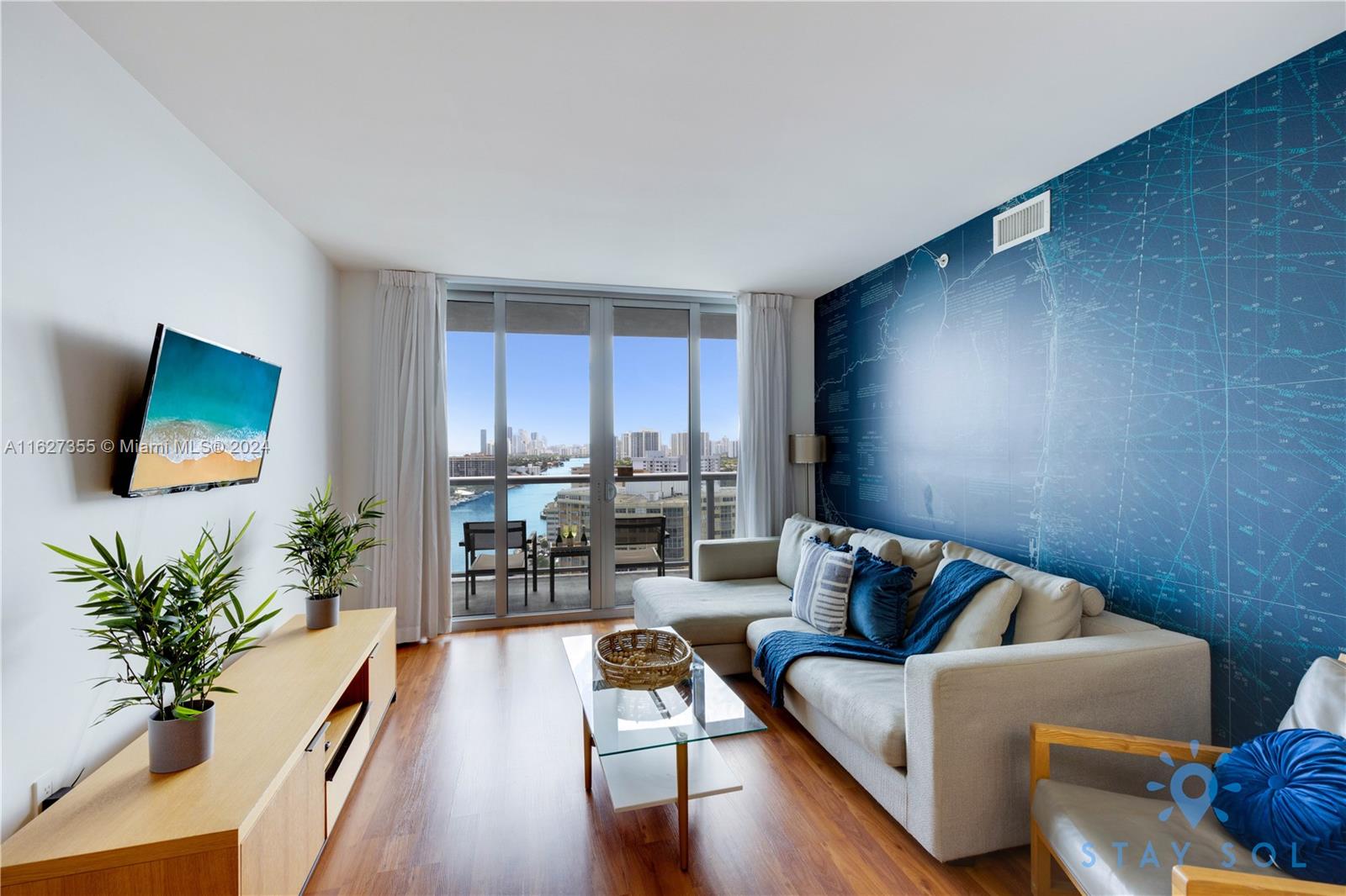 A living room features a blue map wall, a sectional sofa, and a balcony with water views — 2602 E Hallandale Beach Blvd # R2009, Hallandale Beach FL 33009, HALLANDALE BEACH, FL
