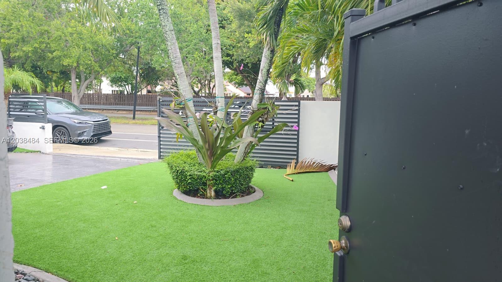 A view of a front yard with artificial grass, a circular planter, and a metal gate — 13220 SW 66th St # A, Miami FL 33183, MIAMI, FL