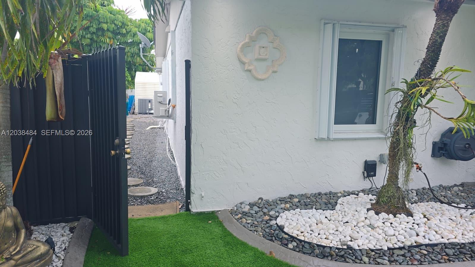 A white stucco exterior wall features a decorative medallion, a window, and a gravel pathway — 13220 SW 66th St # A, Miami FL 33183, MIAMI, FL