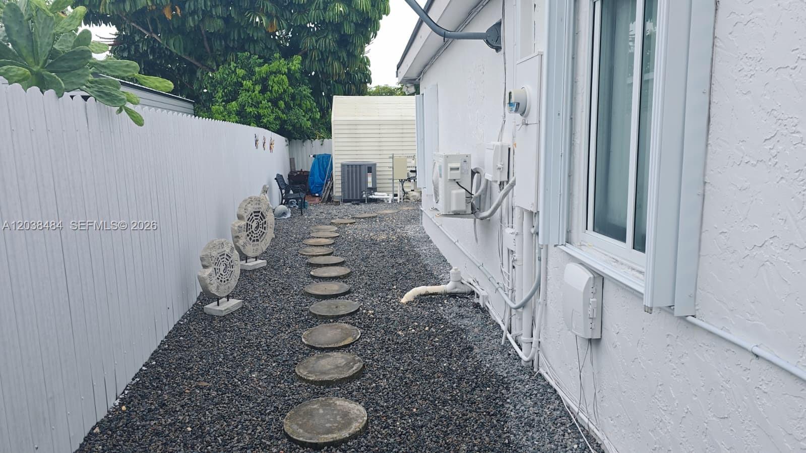 A gravel side yard features a stone path, decorative circular ornaments, and exterior wall equipment — 13220 SW 66th St # A, Miami FL 33183, MIAMI, FL