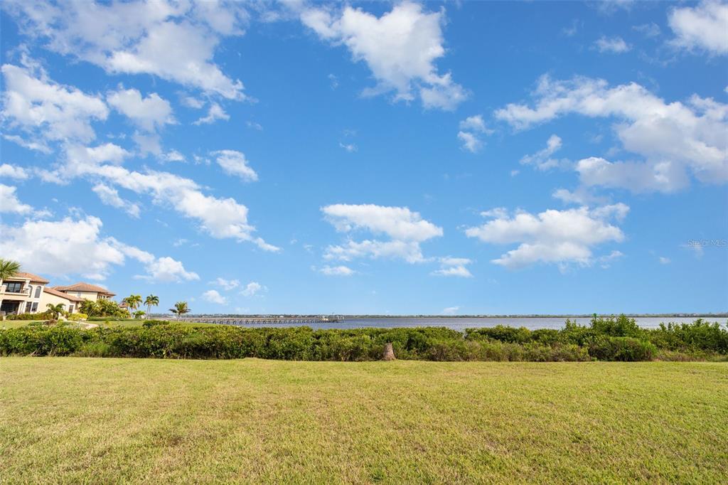 A grassy lawn overlooks a body of water with a distant pier and houses — 3528 FOX TERRACE, PORT CHARLOTTE, FL