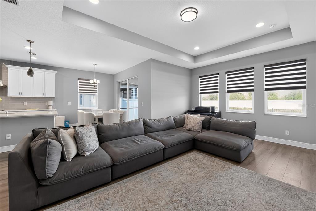 A living room features a large gray sectional sofa, wood flooring, and a tray ceiling — 3663 QUIET DRIVE, SARASOTA, FL