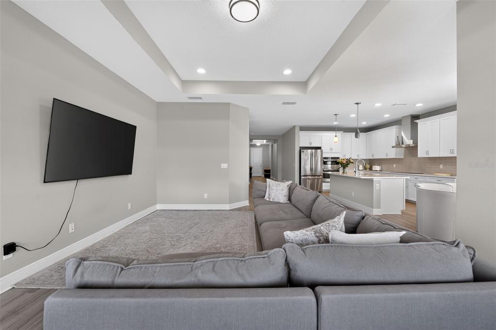 A living room with a gray sectional sofa faces a wall-mounted television and open kitchen — 3663 QUIET DRIVE, SARASOTA, FL