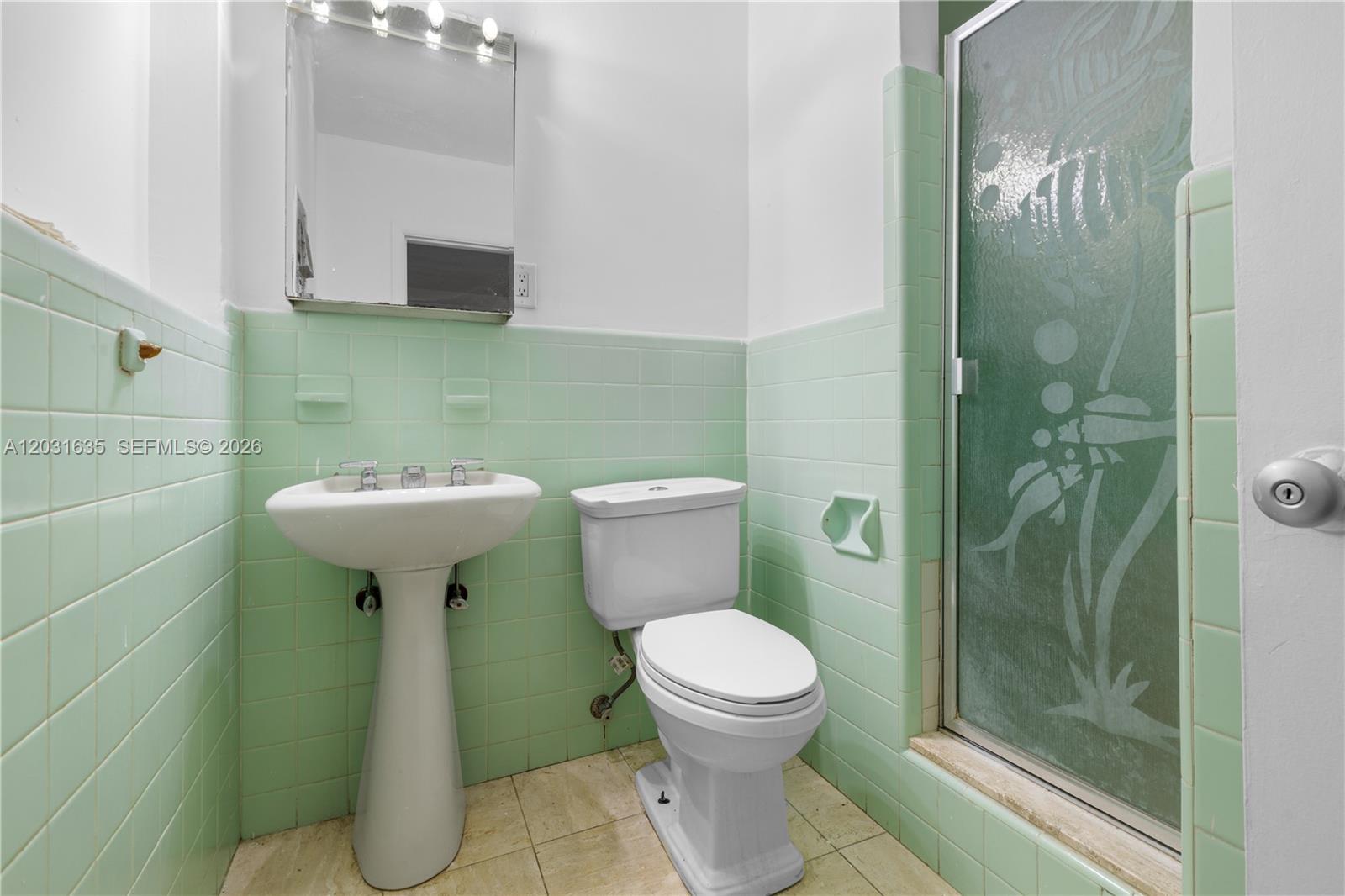 A bathroom features a pedestal sink, white toilet, and light green tiled walls — 3061 NE 4th Ave, Wilton Manors FL 33334, WILTON MANORS, FL