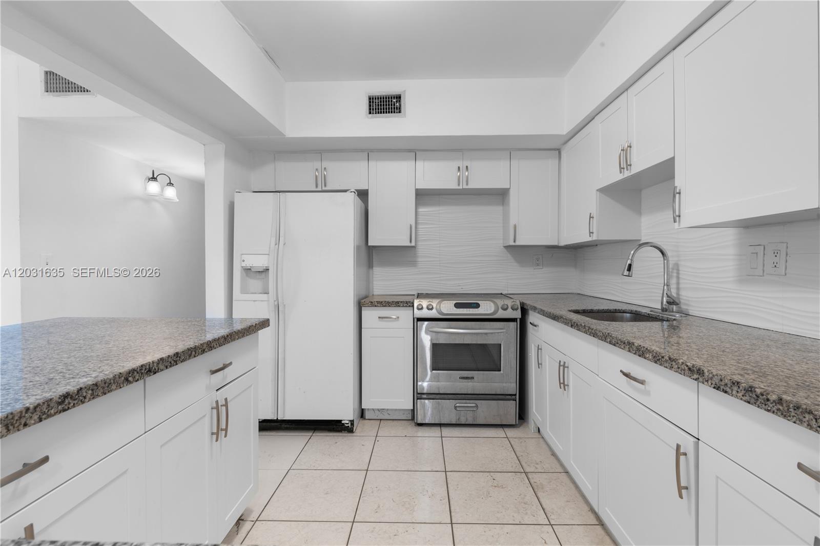 A kitchen features white cabinetry, granite countertops, stainless steel appliances, and light-colored tile flooring — 3061 NE 4th Ave, Wilton Manors FL 33334, WILTON MANORS, FL