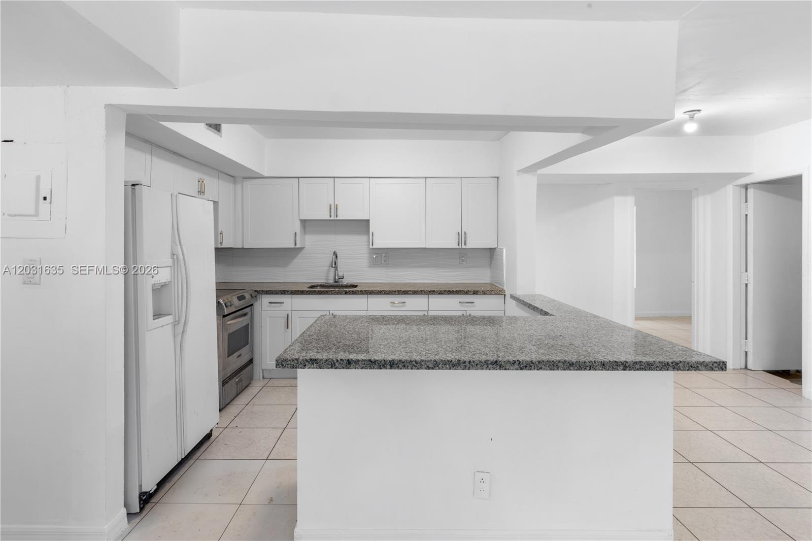 A kitchen features white cabinets, granite countertops, and a peninsula island on tiled floors — 3061 NE 4th Ave, Wilton Manors FL 33334, WILTON MANORS, FL