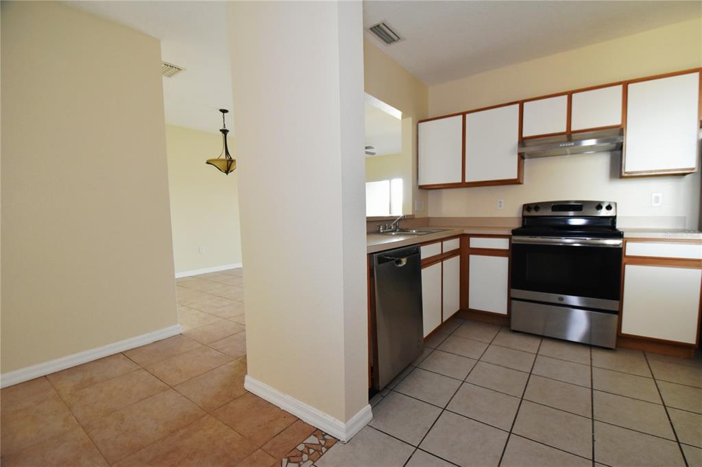 A kitchen with white cabinets, stainless steel appliances, and tile flooring, adjacent to a dining area — 9612 SEADALE COURT UNIT 201, RIVERVIEW, FL