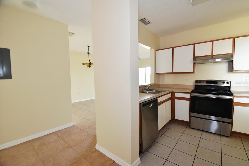 A kitchen with white cabinets, stainless steel appliances, and tiled floors next to a dining area — 9612 SEADALE COURT UNIT 201, RIVERVIEW, FL