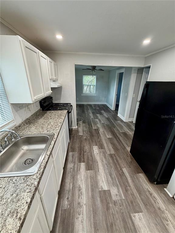 A kitchen with white cabinets, granite-look countertops, and a black refrigerator leads to a room — 908 BEVERLY AVENUE UNIT F, LARGO, FL