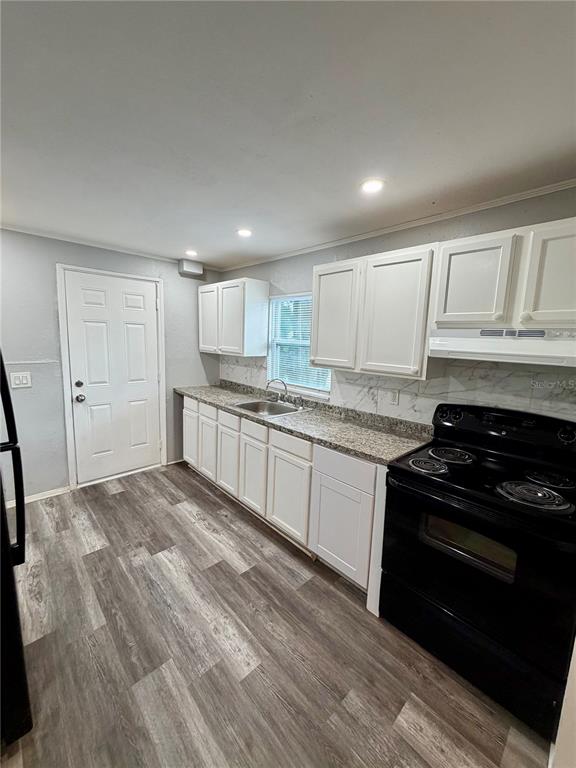 A kitchen with white cabinets, granite countertops, a black stove, and wood-look flooring — 908 BEVERLY AVENUE UNIT F, LARGO, FL