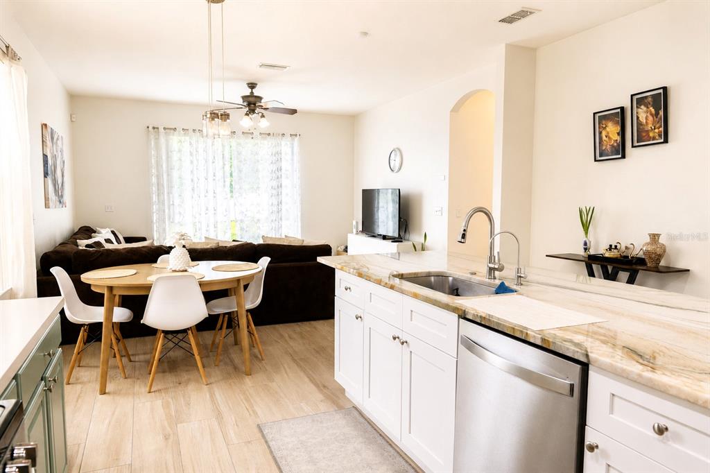 A kitchen with white cabinets and stone countertops overlooks a dining area and living room — 10118 CYPRESS KNEE CIRCLE, ORLANDO, FL