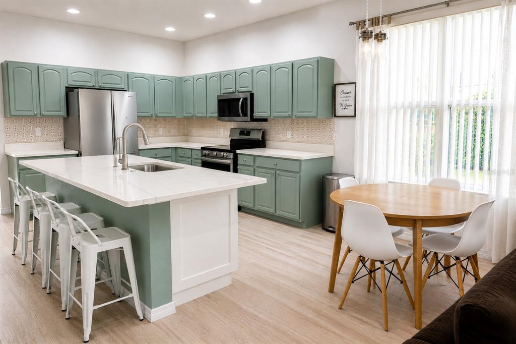 A kitchen features sage green cabinets, a white quartz island, and a small dining area — 10118 CYPRESS KNEE CIRCLE, ORLANDO, FL
