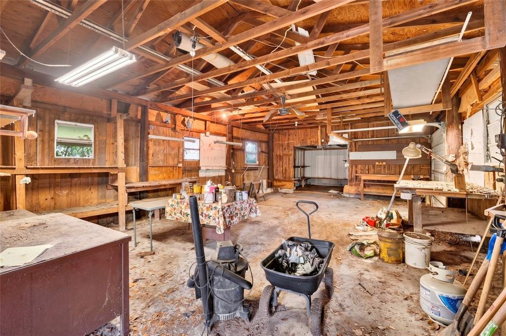 A rustic, unfinished workshop features exposed wooden rafters, a concrete floor, and various workbenches — 6141 SE BABB ROAD, BELLEVIEW, FL