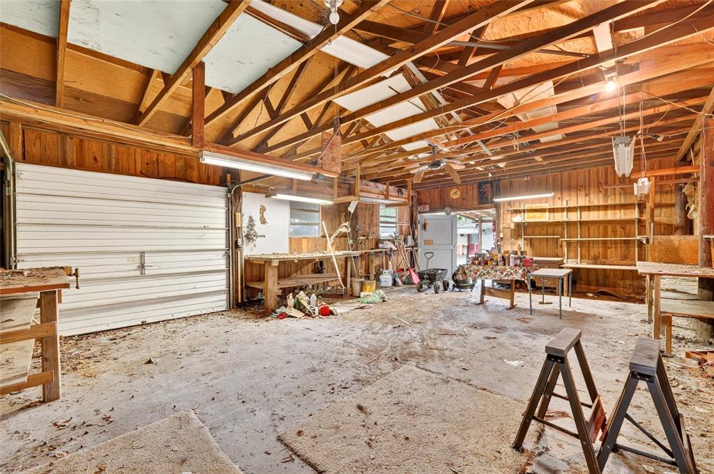 A rustic, unfinished garage with exposed wood rafters, concrete flooring, and various workbenches — 6141 SE BABB ROAD, BELLEVIEW, FL