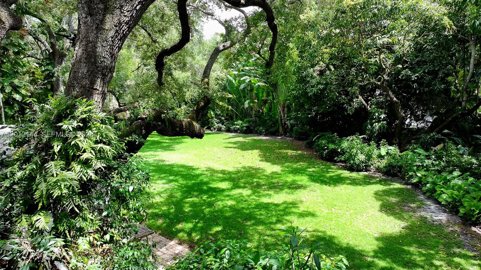 A lush green lawn is surrounded by mature trees and dense tropical landscaping — 530 Melaleuca Ln, Miami FL 33137, MIAMI, FL