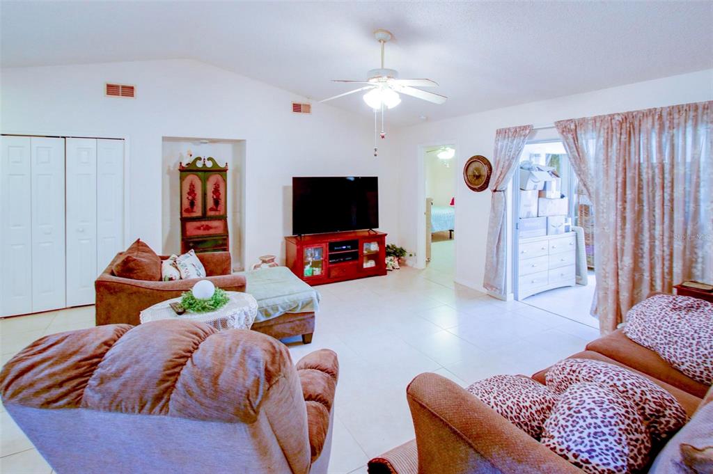 A living room features tile flooring, a ceiling fan, a television, and brown upholstered furniture — 7403 HEATHER WALK DRIVE, WEEKI WACHEE, FL