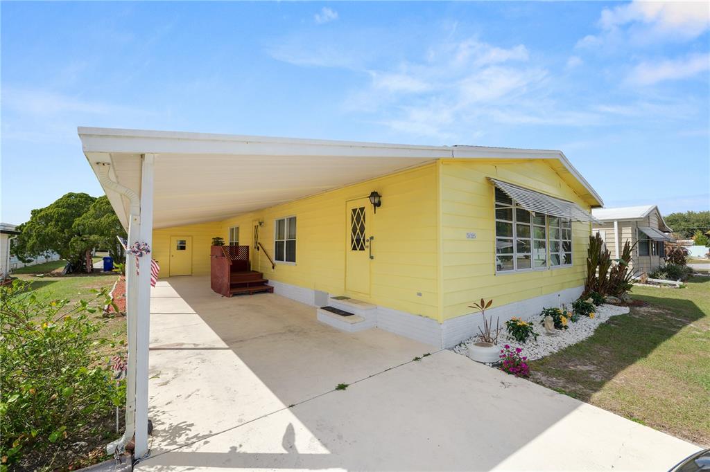 A yellow mobile home features a large carport, a concrete driveway, and a small garden bed — 5026 FOXWOOD BOULEVARD, LAKELAND, FL