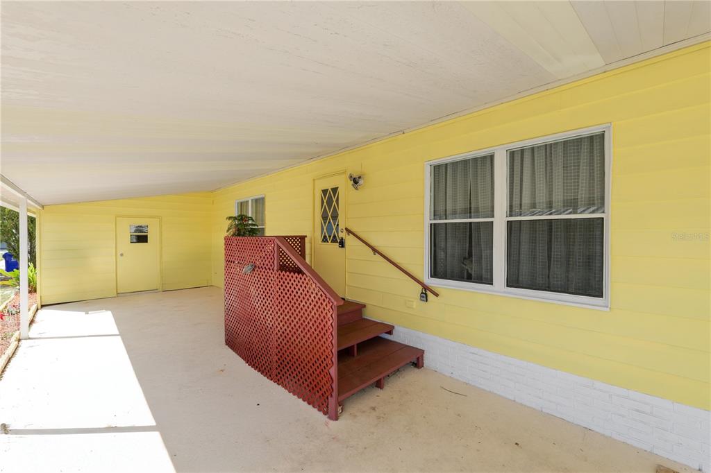 A yellow house exterior features a covered patio, a red lattice railing, and wooden steps — 5026 FOXWOOD BOULEVARD, LAKELAND, FL
