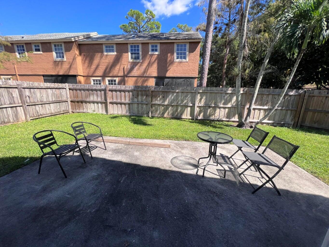 A concrete patio with outdoor furniture sits in a backyard enclosed by a wooden fence — 1598 Hawthorne Place, Wellington FL 33414, WELLINGTON, FL