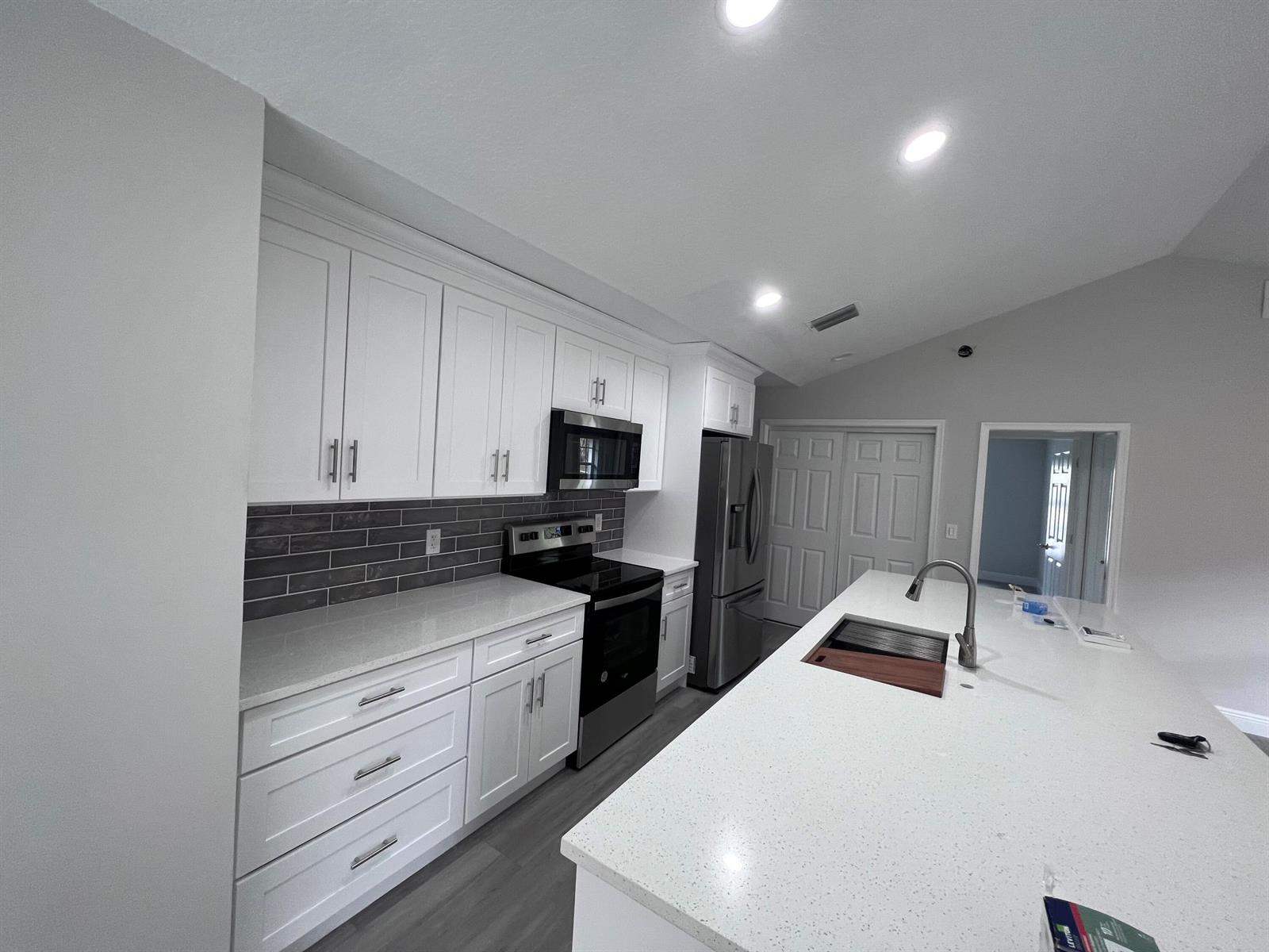 A modern kitchen features white cabinets, quartz countertops, a gray tile backsplash, and a large island — 1598 Hawthorne Place, Wellington FL 33414, WELLINGTON, FL