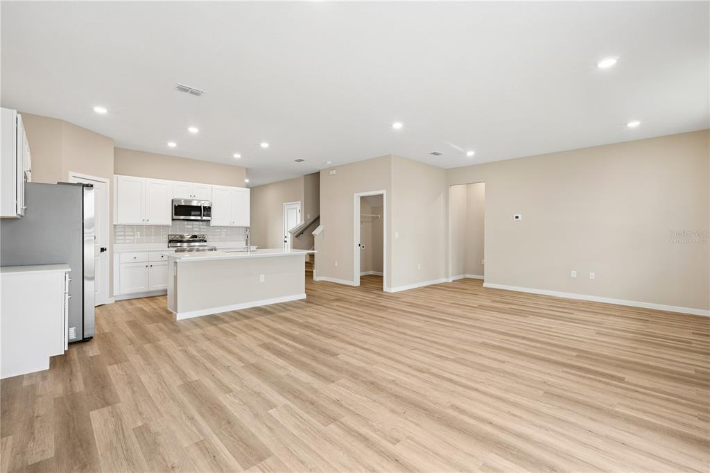 An open-concept kitchen and living area featuring white cabinets, stainless appliances, and light wood flooring — 90 SPRINGWOOD DRIVE, PALM COAST, FL