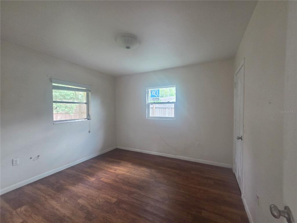 An empty bedroom features wood-look flooring, white walls, two windows, and a closed door — 572 BELL, BROOKSVILLE, FL