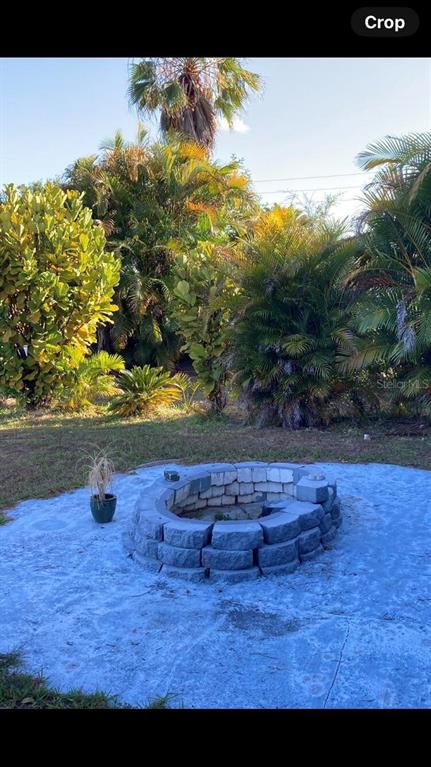 A stone fire pit sits on a circular concrete patio surrounded by lush tropical landscaping — 303 COCOA COURT, KISSIMMEE, FL