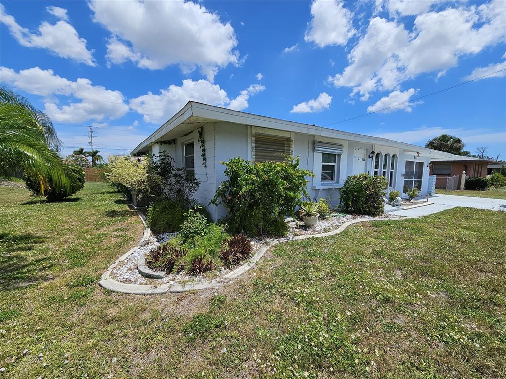 A single-story house with a white exterior, a curved garden bed, and a grassy yard — 531 AZALEA DRIVE NW, PORT CHARLOTTE, FL