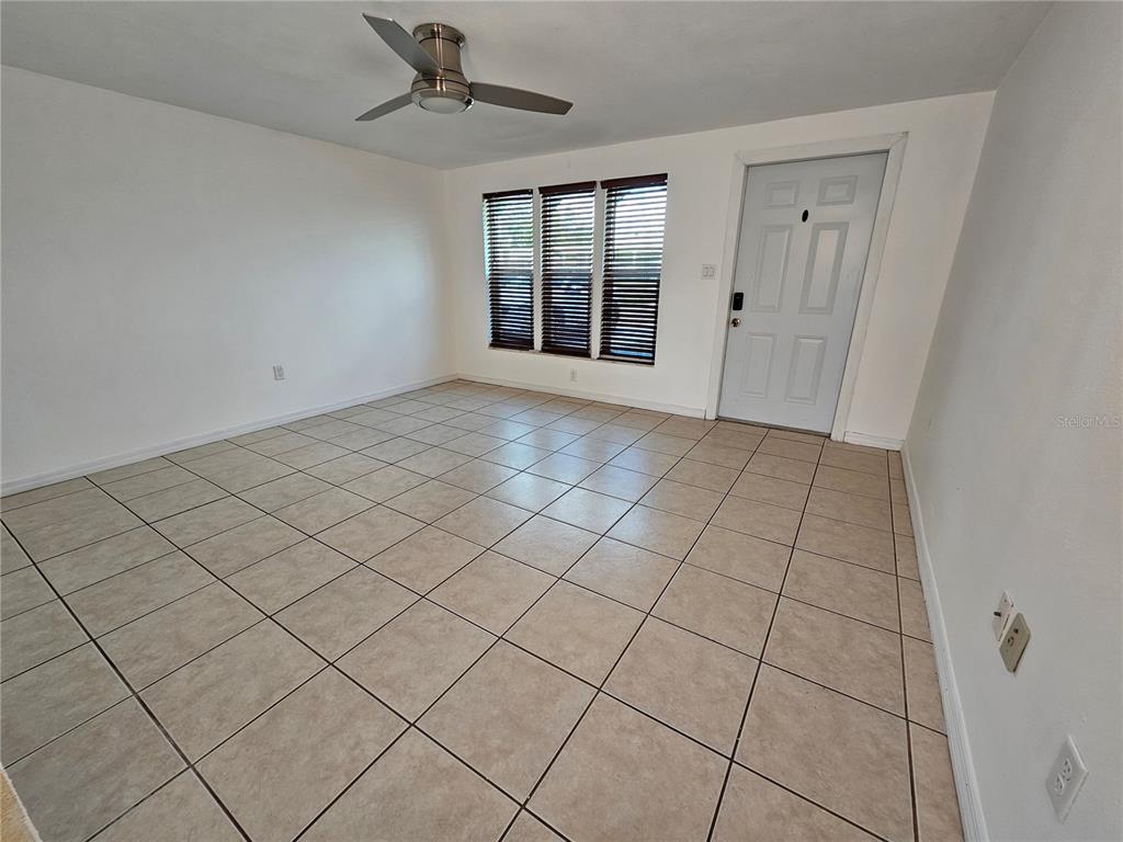 An empty room features light-colored tile flooring, white walls, a ceiling fan, and a door — 531 AZALEA DRIVE NW, PORT CHARLOTTE, FL
