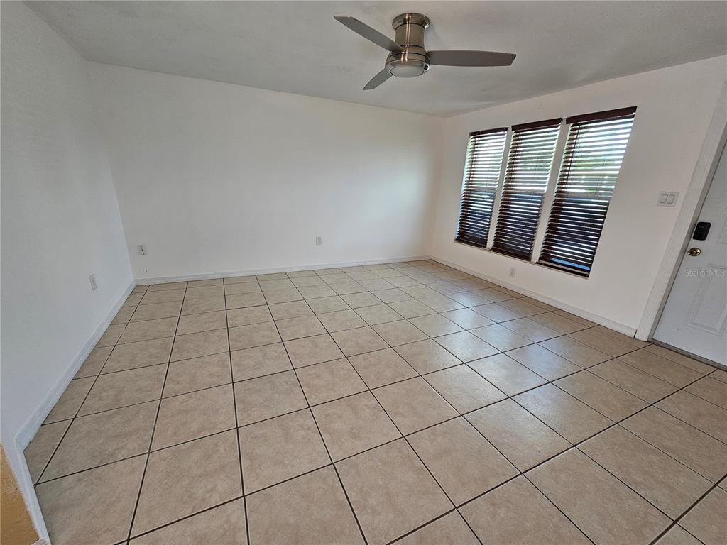 An empty room features white walls, beige tile flooring, and a ceiling fan — 531 AZALEA DRIVE NW, PORT CHARLOTTE, FL