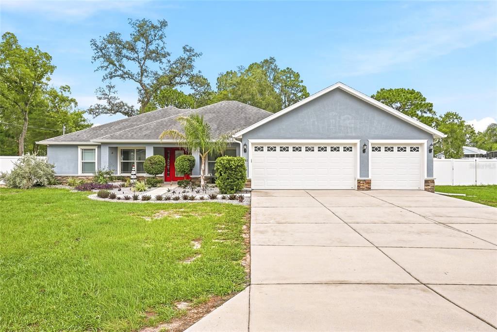 A single-story house with a blue exterior, a three-car garage, and a red front door — 1180 BATTERSEA AVENUE, SPRING HILL, FL