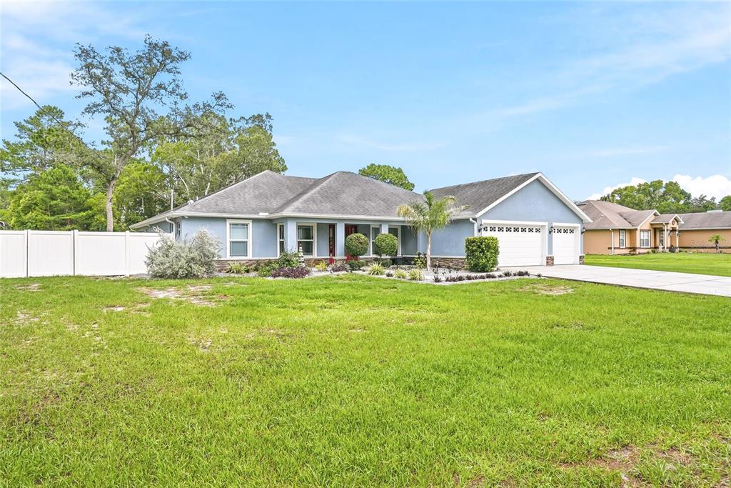 A light blue single-story house with a two-car garage and a white vinyl fence — 1180 BATTERSEA AVENUE, SPRING HILL, FL