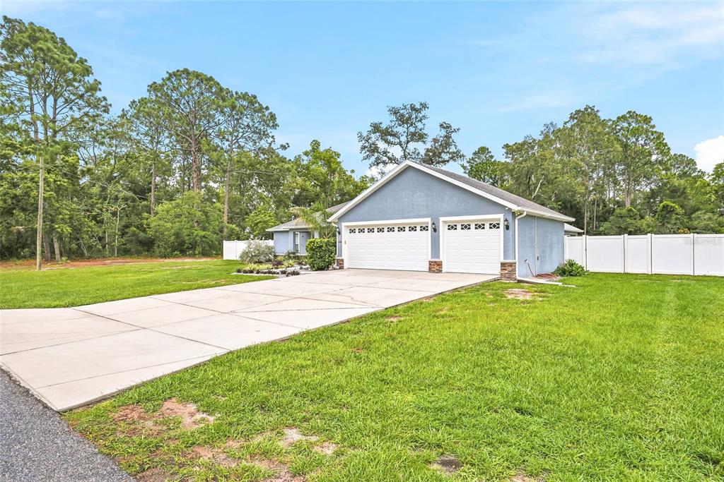 A blue house with a three-car garage and a concrete driveway sits on a lawn — 1180 BATTERSEA AVENUE, SPRING HILL, FL