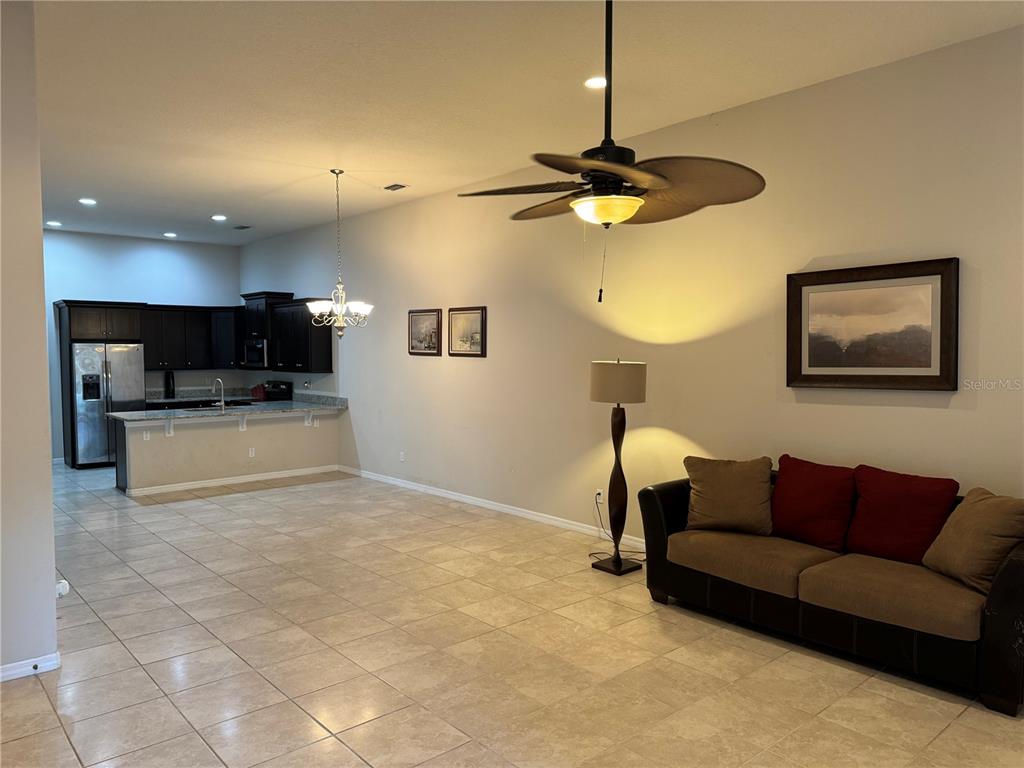 A living room with tile floors, a ceiling fan, and an open kitchen with dark cabinets — 3422 TORRE BOULEVARD, NEW SMYRNA BEACH, FL