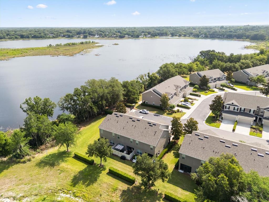 An aerial view shows townhomes situated next to a large lake and green space — 1512 GROUNDSEL LANE, OCOEE, FL