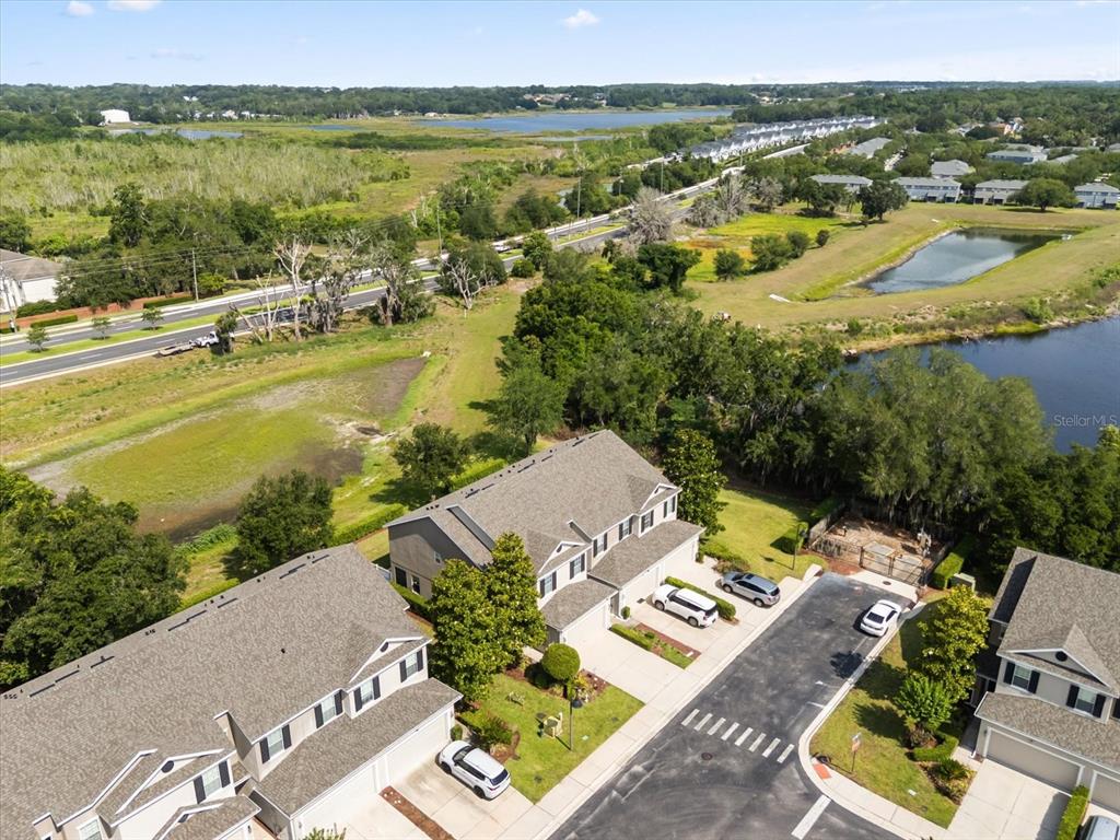 An aerial view shows townhomes with gray roofs, driveways, and surrounding green space and water — 1512 GROUNDSEL LANE, OCOEE, FL