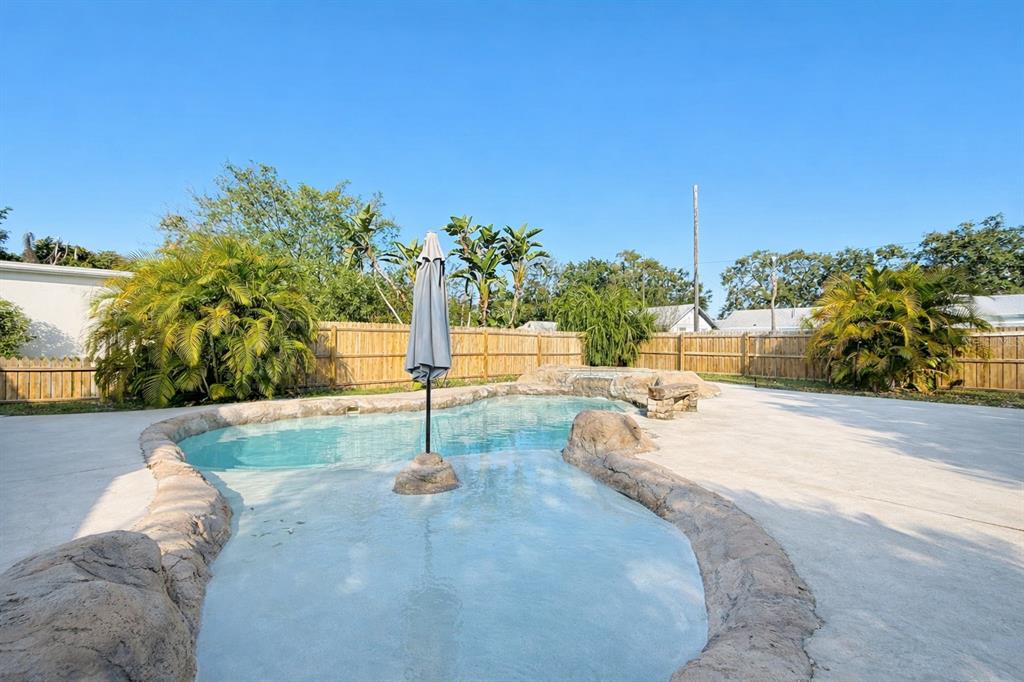 A backyard features a freeform swimming pool with a rock border and a central umbrella — 5613 19TH AVENUE S, GULFPORT, FL