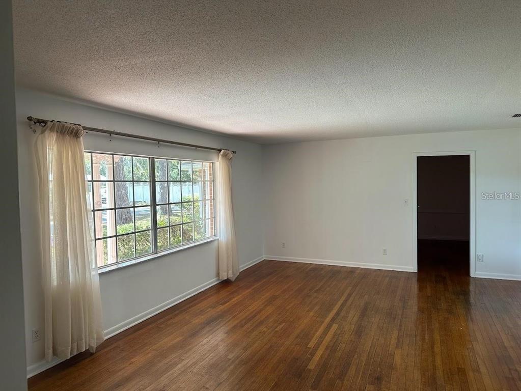 An empty room with hardwood floors, white walls, and a large window with sheer curtains — 1333 SE 17TH STREET, OCALA, FL