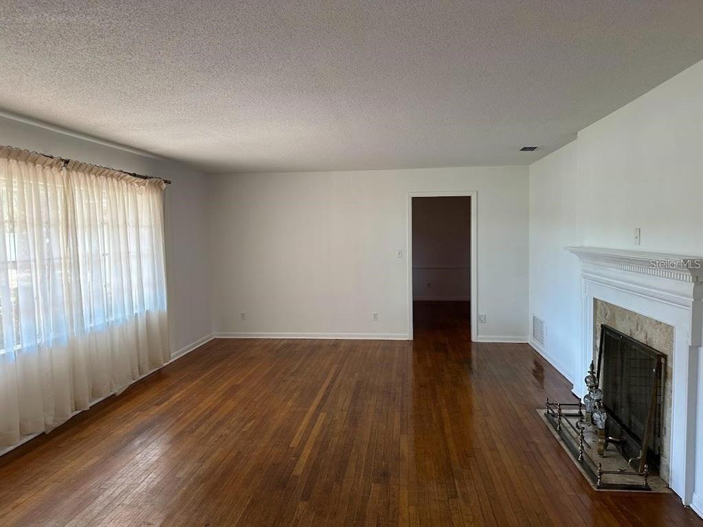 A living room with hardwood floors, a fireplace, and a large window with sheer curtains — 1333 SE 17TH STREET, OCALA, FL