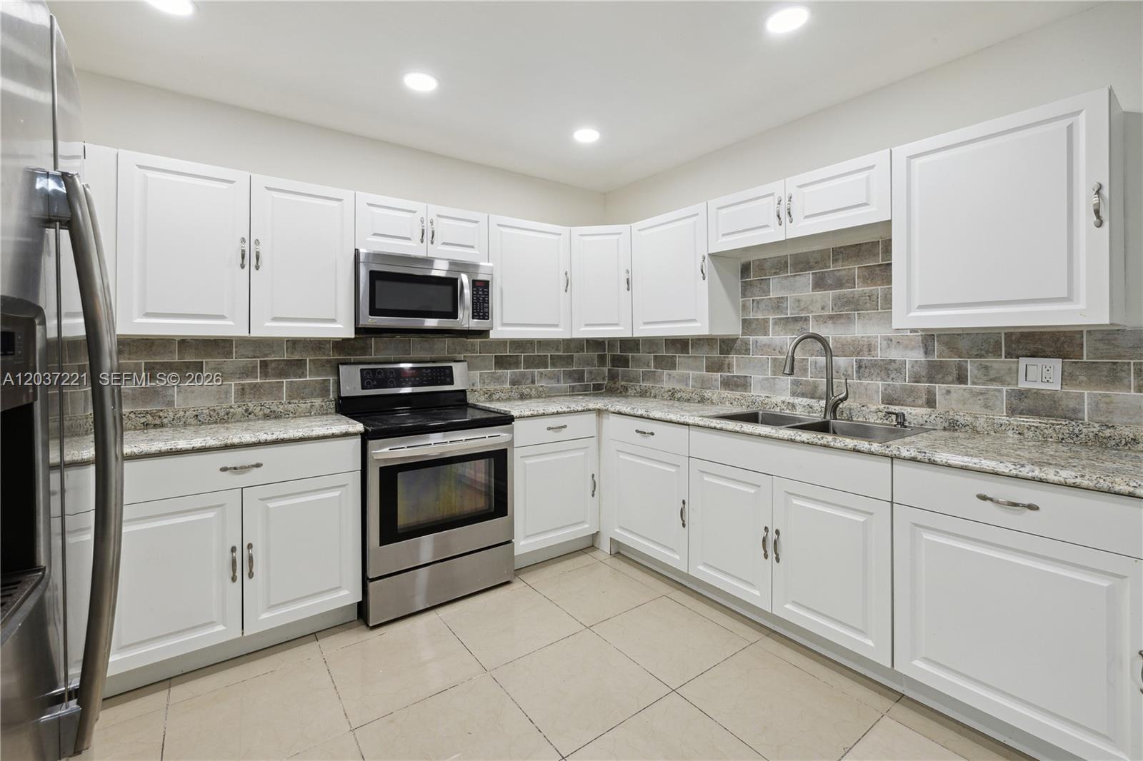 A kitchen features white cabinets, granite countertops, a tiled backsplash, and stainless steel appliances — 15131 SW 58th St, Miami FL 33193, MIAMI, FL