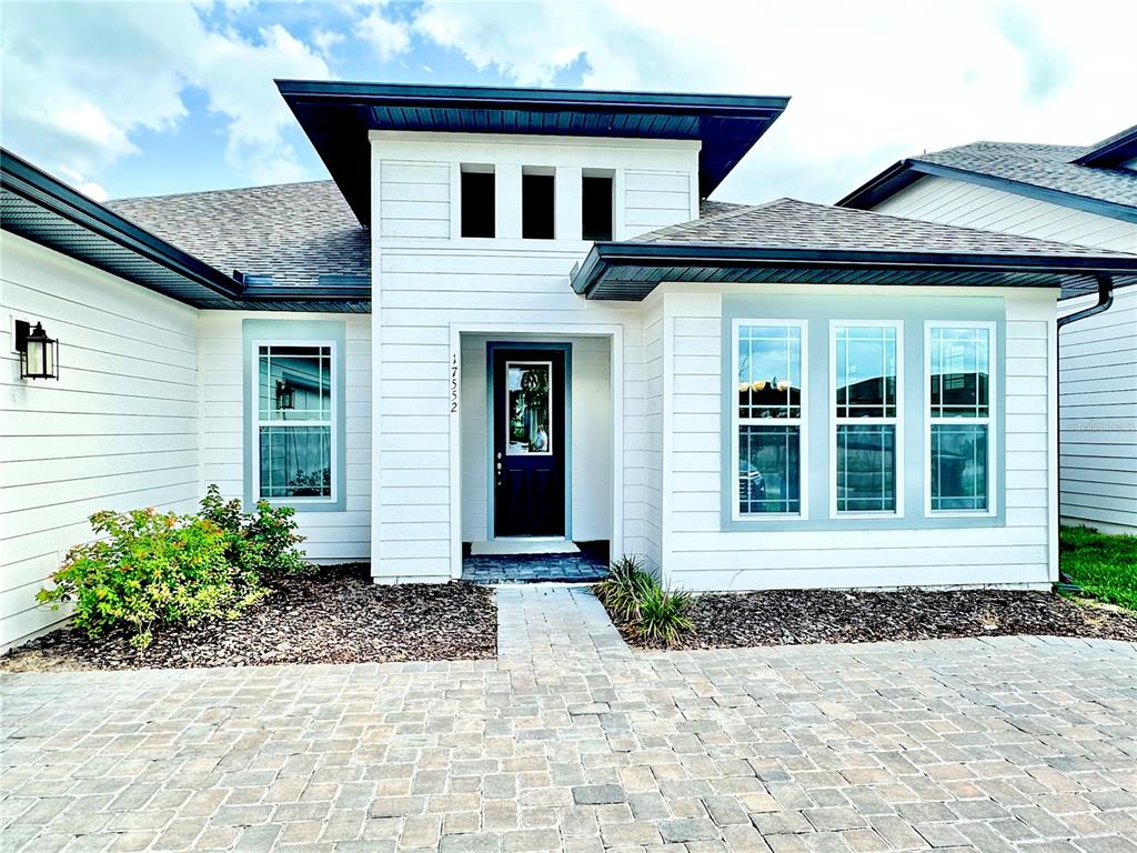 A modern white house exterior features a dark front door and a paver driveway — 17552 LAKE STAR ROAD, WINTER GARDEN, FL