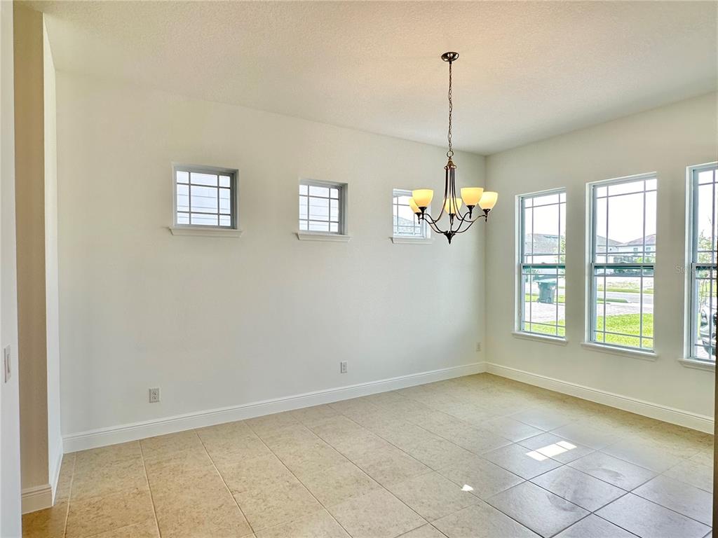 An empty dining room features tile flooring, a chandelier, and multiple windows on two walls — 17552 LAKE STAR ROAD, WINTER GARDEN, FL
