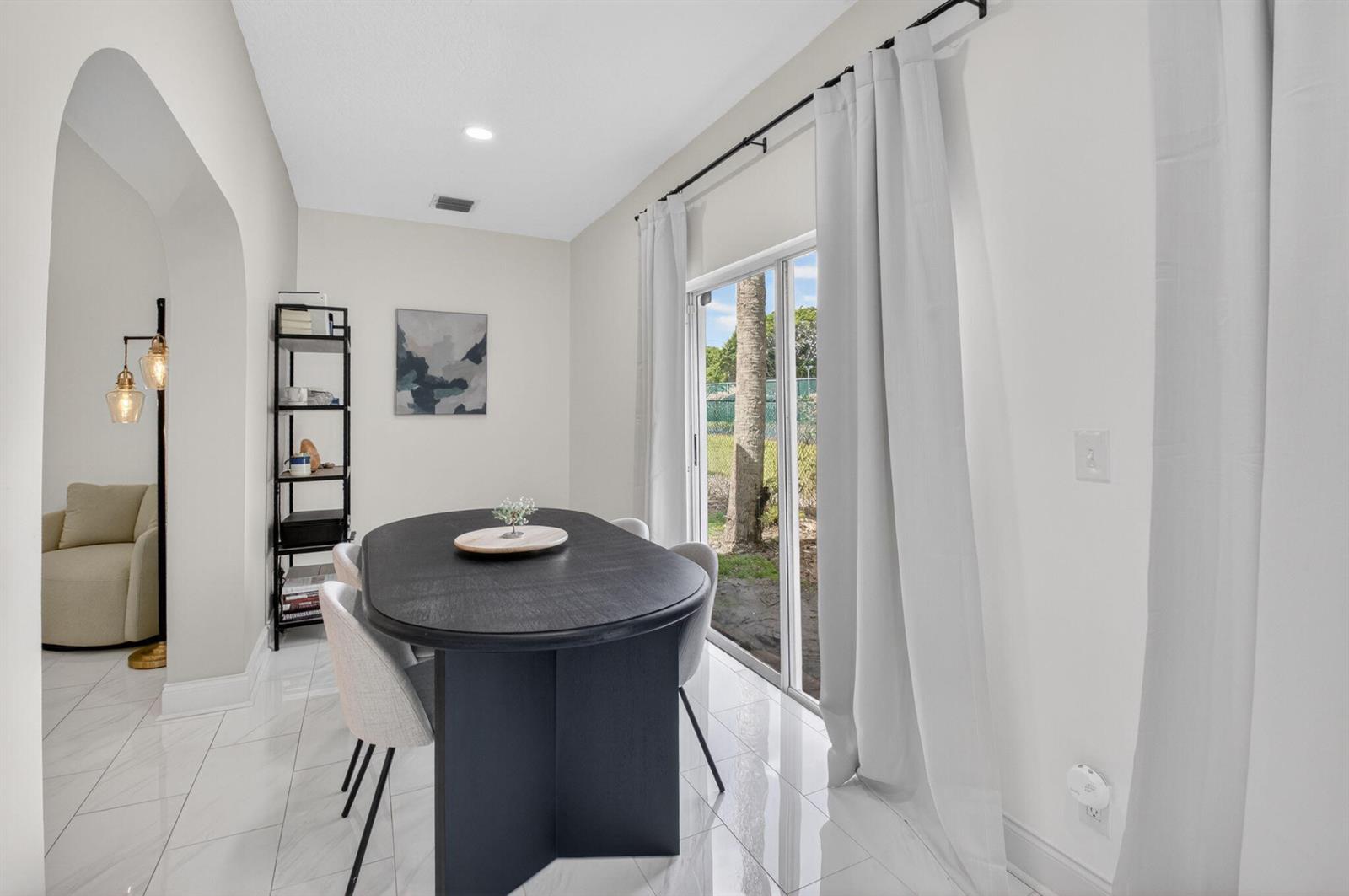 A dining room features a black oval table, light-colored chairs, and a sliding glass door — 5111 Sabal Gardens Lane # 4, Boca Raton FL 33487, BOCA RATON, FL